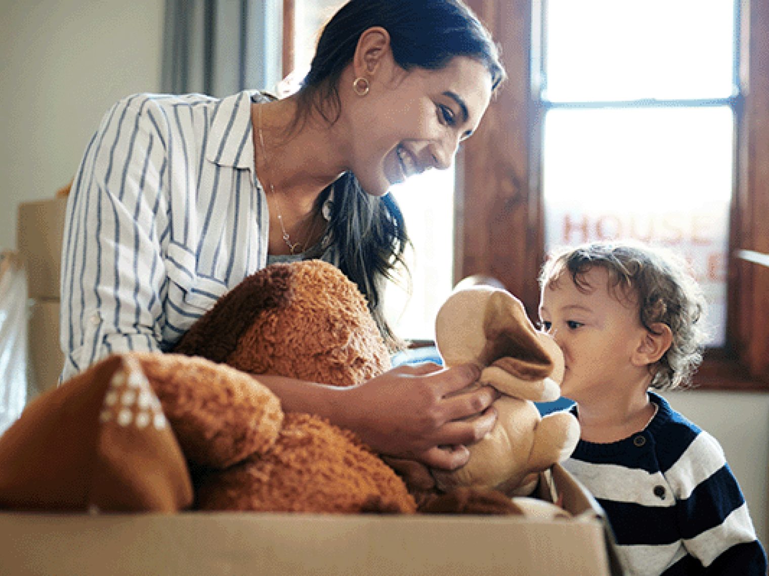 A mother and her young child unpacking a box of toys in a brightly lit room.