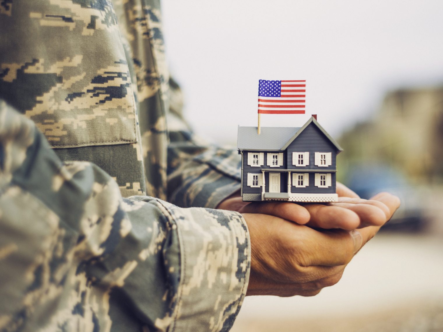 Servicemember holding a small wooden house model with an American Flag on it.