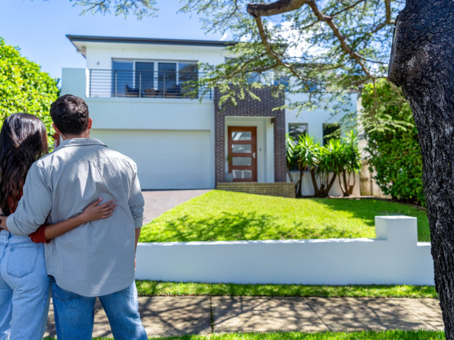 The back of a young couple standing in front of a home.