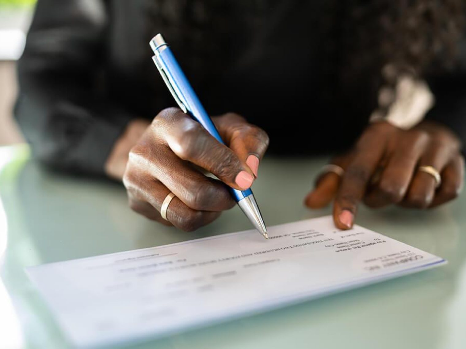 A man's hands prepare to write on a check with a gold pen.