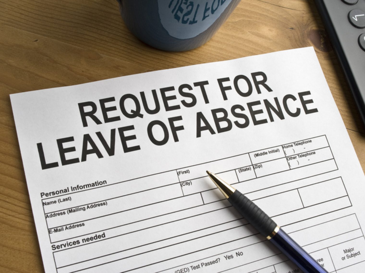 A 'Request for Leave of Absence' form on a wooden desk, with a pen on top, next to a mug and a phone.