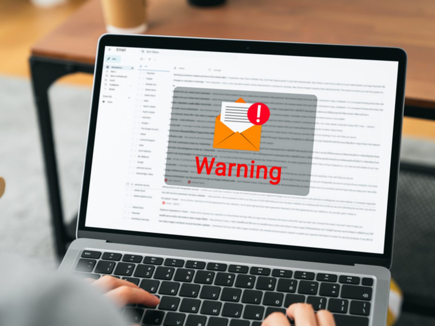 A person's view over a laptop screen displaying an email interface with a prominent "Warning" alert.