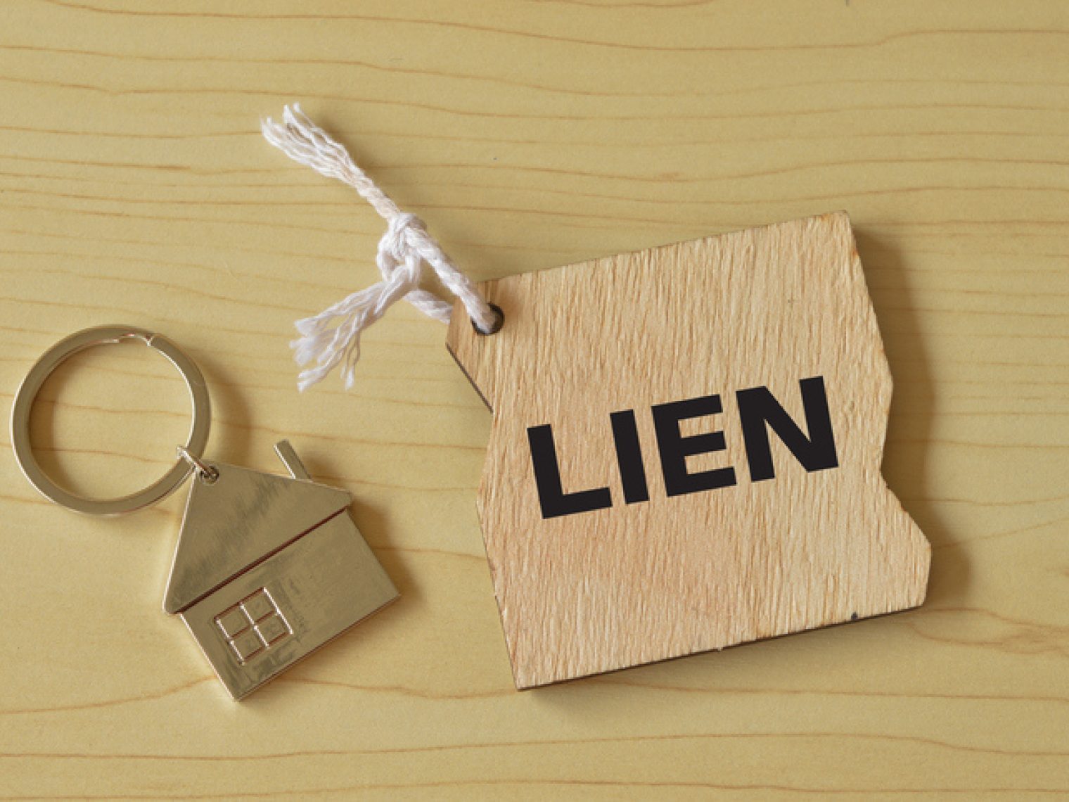 A house-shaped keyring next to a tag with the word "LIEN" on it, placed on a wooden surface.