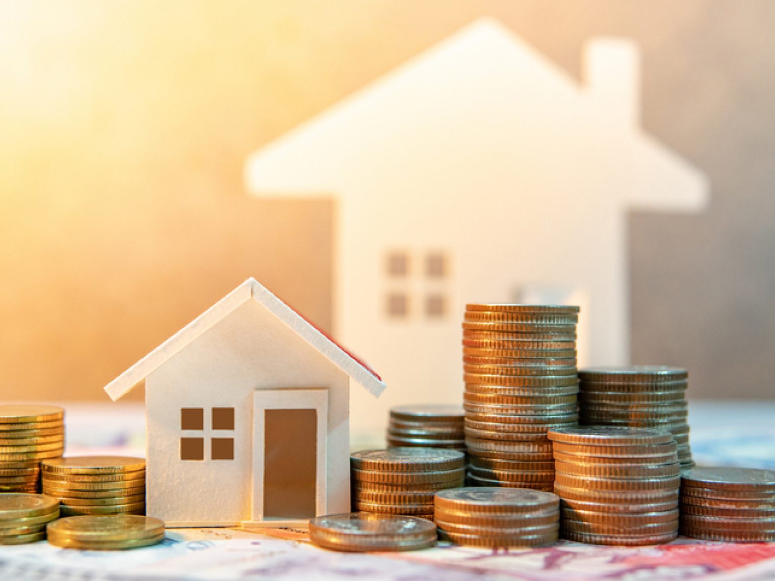 Image with a white model house next to rising stacks of coins.