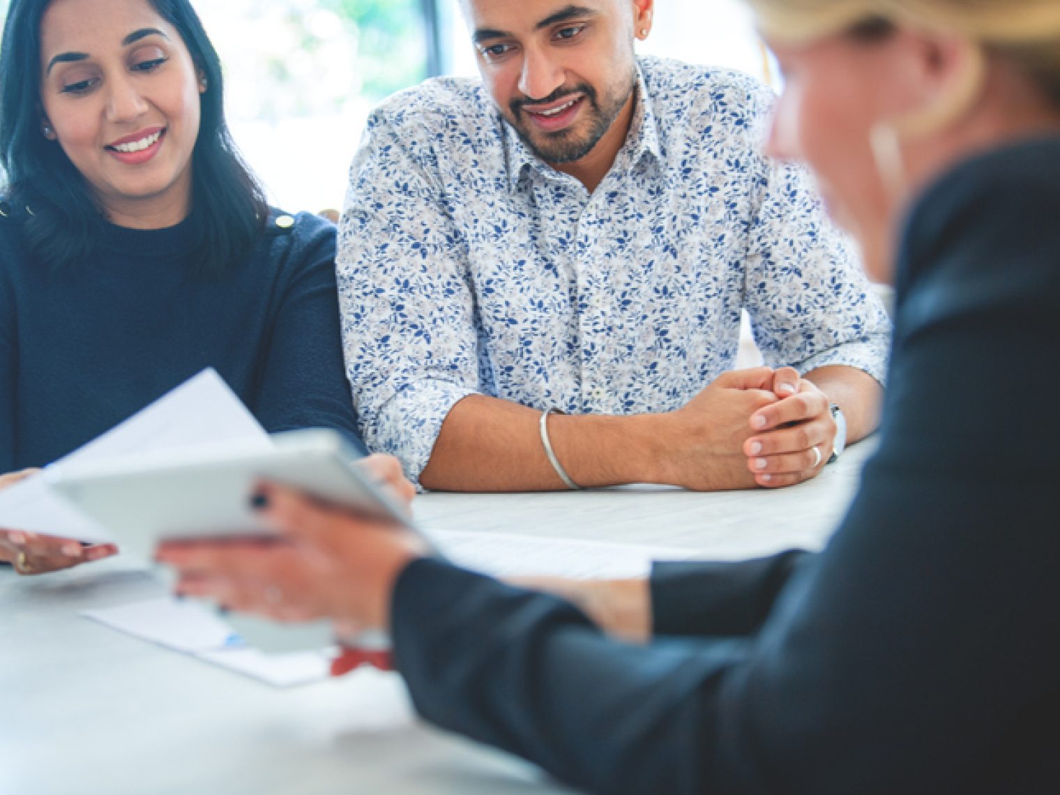 A cheerful couple attentively listens to a real estate agent, who is presenting a document during a meeting.