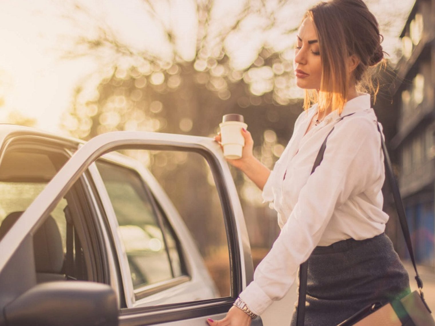 Woman holding coffee cup opens car door.